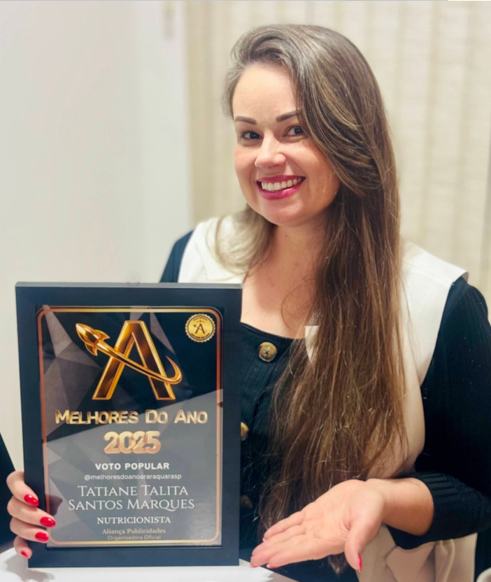 Tatiane Santos sorrindo, de cabelo longo, segurando uma placa de premiação